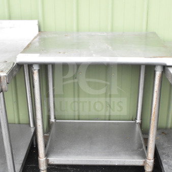 Commercial metal table with under shelf, noticeable wear and rust on legs, suitable for practical use.