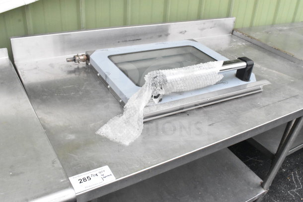 Commercial stainless steel table with under shelf, equipped with can opener mount and oven door. Auction tag visible.