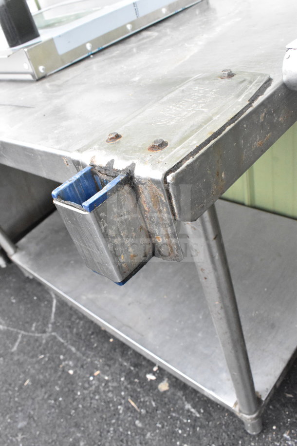 Commercial table with under shelf, mounted can opener attachment, and oven door. Metal construction, worn condition.