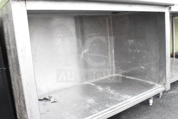 Commercial table with under shelf, stainless steel, visible wear and scratches, suitable for kitchen or industrial use.