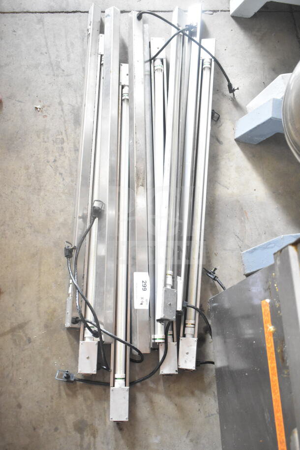 11 metal lights with cords, stacked on concrete floor. Label marked "299." Auction item, "11 Lights. 11 Times Your Bid!"