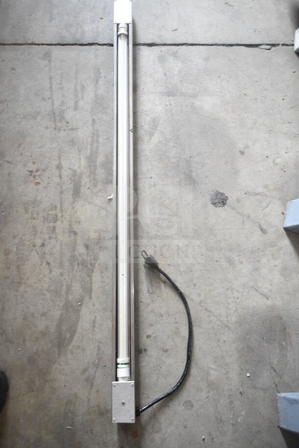 Long fluorescent light fixture with attached power cord on concrete floor; auction lot of 11 lights.