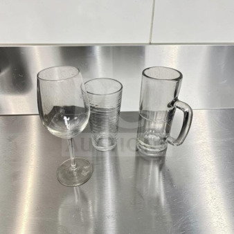 Three types of glassware on a stainless steel surface: a wine glass, a tumbler, and a beer mug. Suitable for restaurant use.