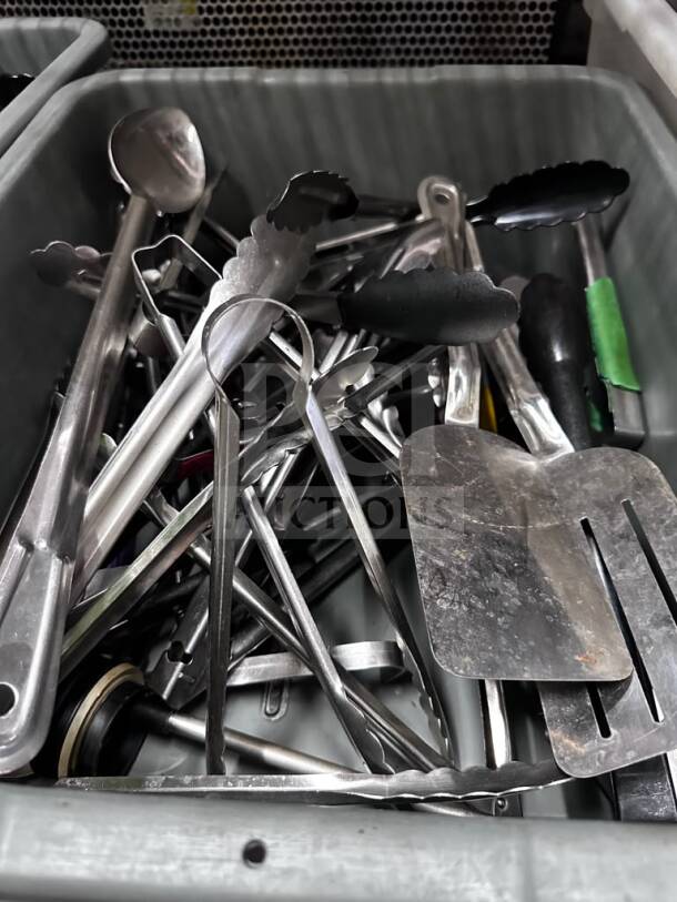 Mixed commercial kitchen utensil lot in containers, featuring tongs, spatulas, ladles, well-maintained, ready for restaurant use.