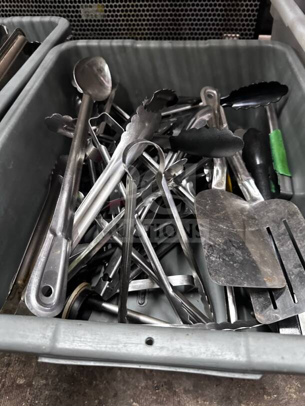 Mixed commercial kitchen utensil lot in gray containers, featuring tongs, spatulas, and ladles. Well-maintained condition.