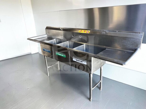 Commercial three-compartment stainless steel sink with dual drainboards, high backsplash, and adjustable legs in flawless condition.