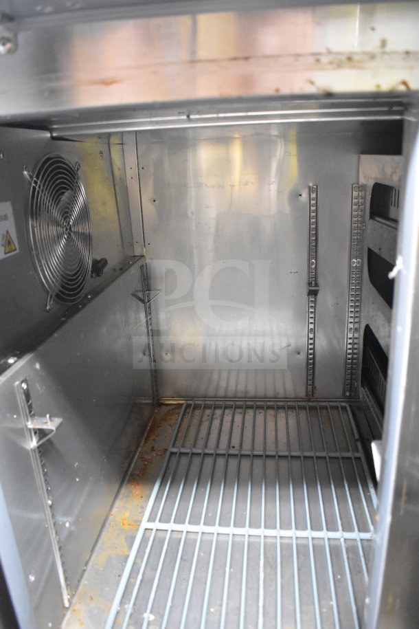 Avantco commercial pizza prep table interior, features shelving and fan, used condition, visible wear and rust on surfaces.