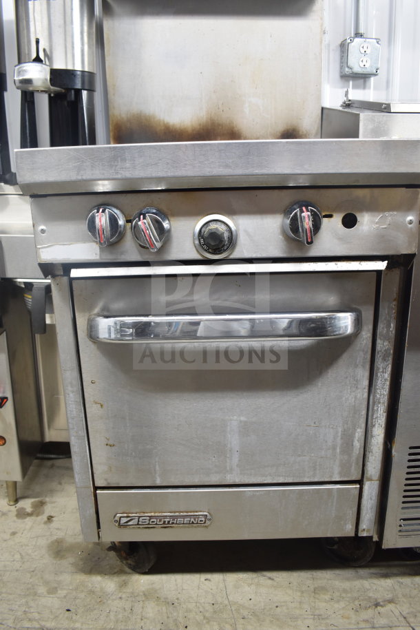 Southbend commercial gas range with 4 burners, oven, overshelf, backsplash, and casters. Signs of use visible.