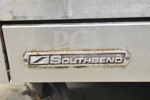 Southbend logo on a commercial gas-powered 4 burner range with oven, over shelf, backsplash, and casters. Signs of wear visible.