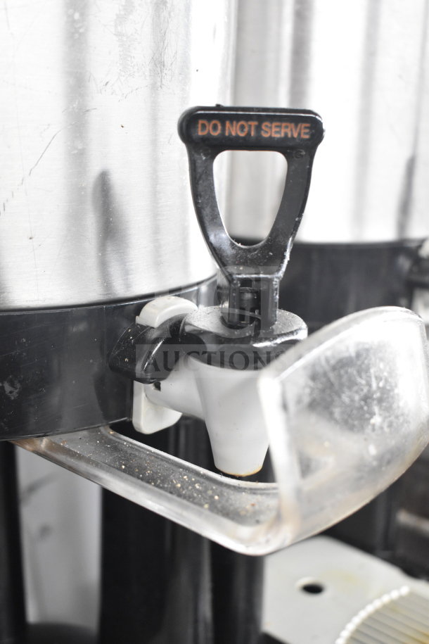 2 Fetco Luxus L3D-10 hot beverage dispensers, stainless steel with black tap, marked "Do Not Serve," in used condition.