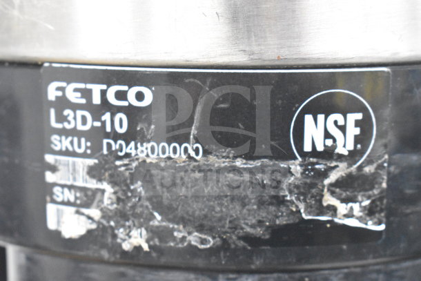 Fetco Luxus L3D-10 hot beverage holder label showing model, SKU, and NSF certification. Peeling surface.
