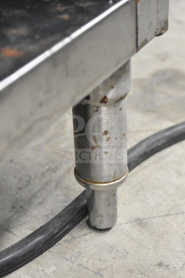 T&P PSL-80-RA2 commercial induction wok range leg detail, shows steel construction with wear, resting on concrete floor.