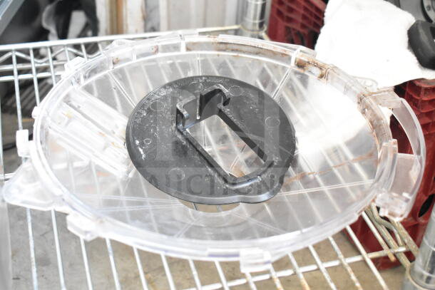 Plastic hopper for drink blending machine on a metal rack. Clear with a black handle, showing wear and light residue.
