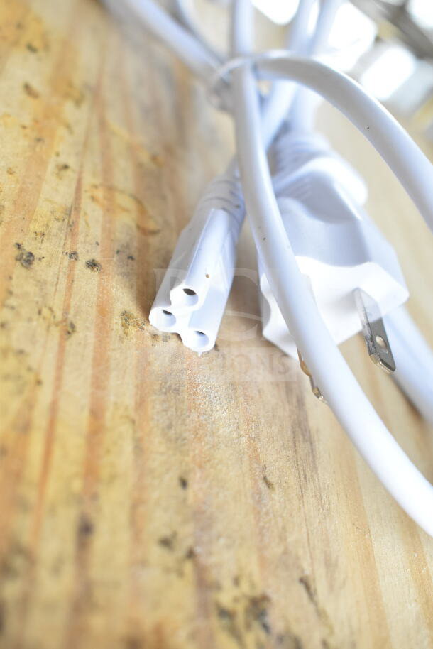 Close-up of a white electrical cord with a three-hole connector and plug, resting on a wooden surface.
