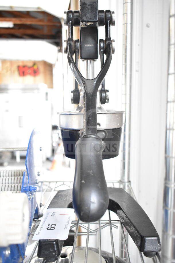 Countertop manual juicer with black handle and sturdy metal construction, in good condition, placed on a wire shelf.