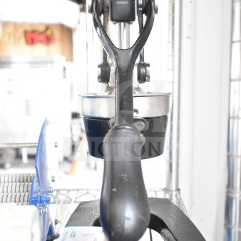Countertop manual juicer with black handle and sturdy metal construction, in good condition, placed on a wire shelf.