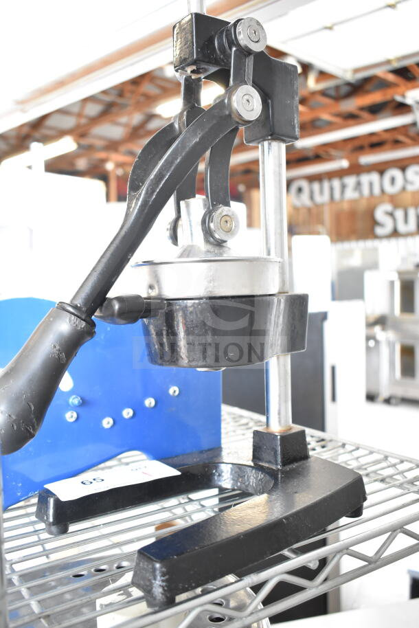 Manual countertop juicer with black metal base and lever, used condition, visible label with auction number.