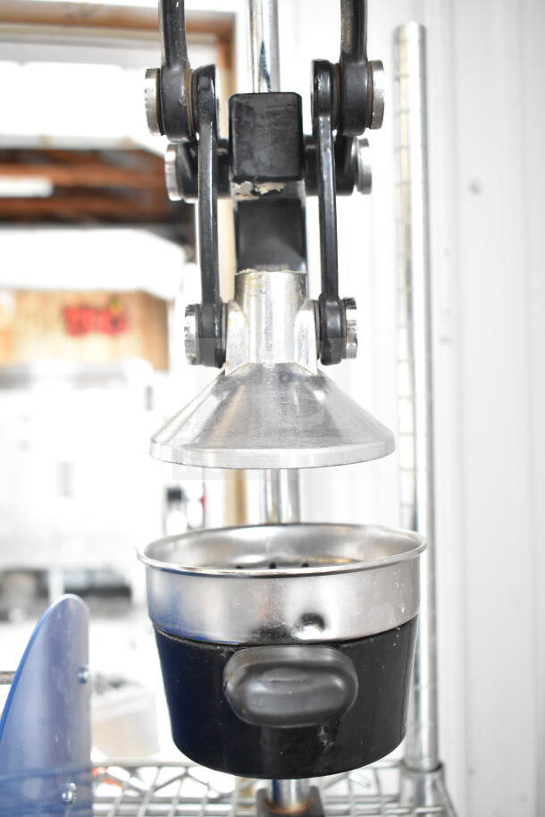 Manual countertop juicer with metallic press and black handle. Good condition, designed for efficient fruit juicing.