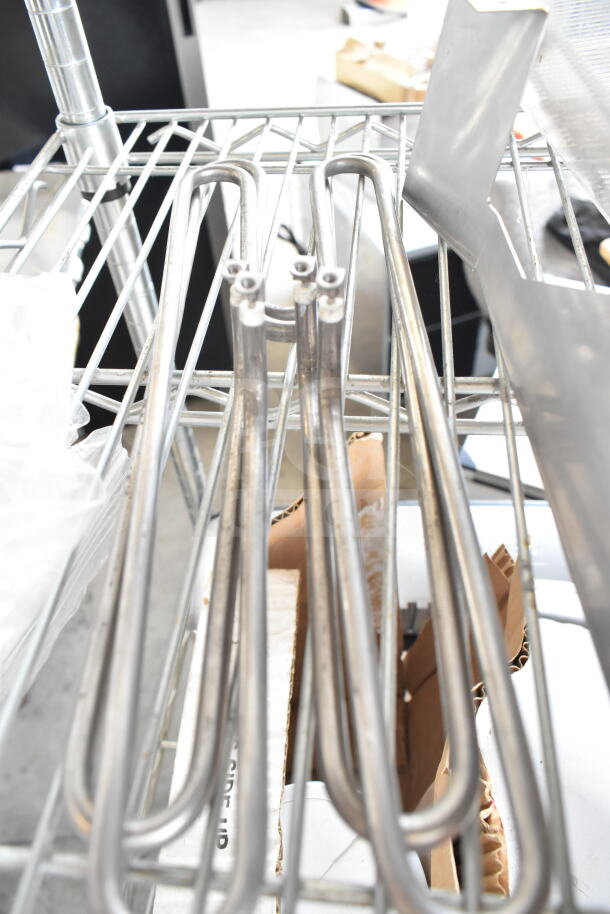 Five assorted metal items on a shelf, including ChocoVision Enrober parts, showing metal coils and brackets.