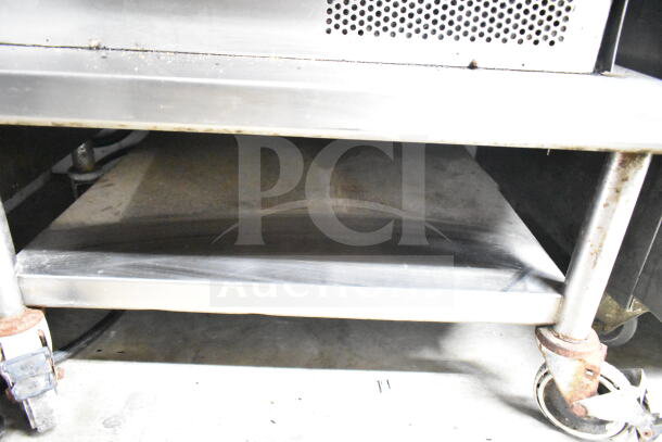 Commercial equipment stand with under shelf and commercial casters. Metal construction, some rust visible on casters, used condition.