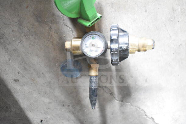 Brass pressure regulator with gauge, black plastic knob, and green cap, in good condition, on concrete surface.