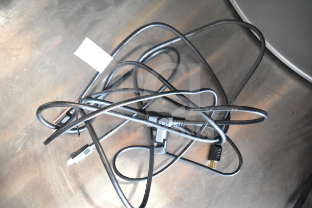 Tangled black power cables on a metal surface, with a small white label attached.