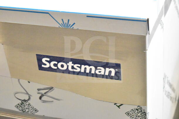 Brand new Scotsman C1030MA-32D ice machine in box; air-cooled, 1077 lb capacity with Scotsman logo visible.