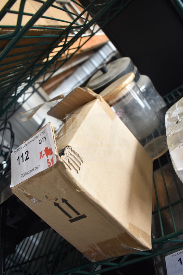Cardboard box with auction label on shelf, containing 5 various items including Taylor thermometers and a container. Box is slightly damaged.