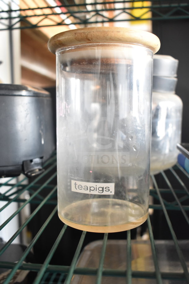 Glass jar with wooden lid, labeled "teapigs", on wire shelf. Part of a lot with Taylor thermometers and container.