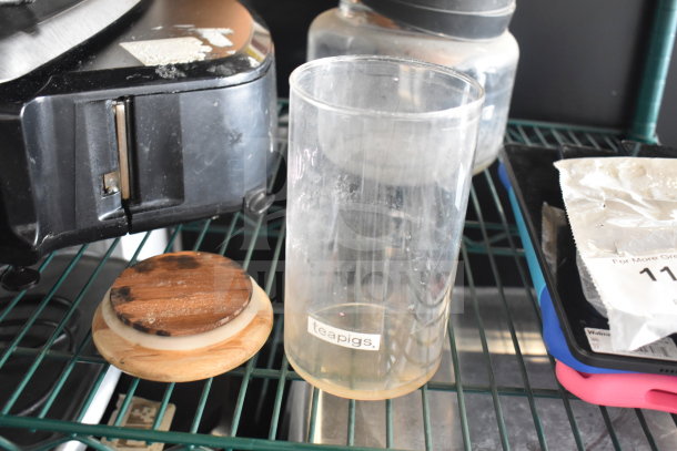 5 various items on shelf; includes Teapigs container, wood lid, black appliance, and foil packet. Vintage condition.