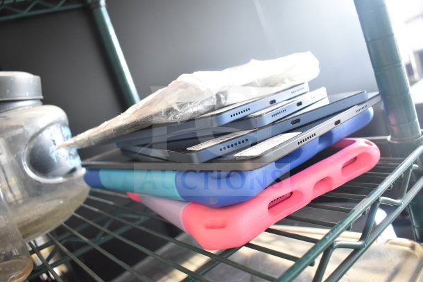 7 Onn tablets stacked, various cases including blue and pink. Tablets appear in fair condition on a wire shelf.