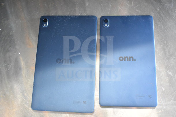 Seven Onn tablets on a table, varying sizes, blue back, rear cameras, Onn logo. Moderate wear visible.