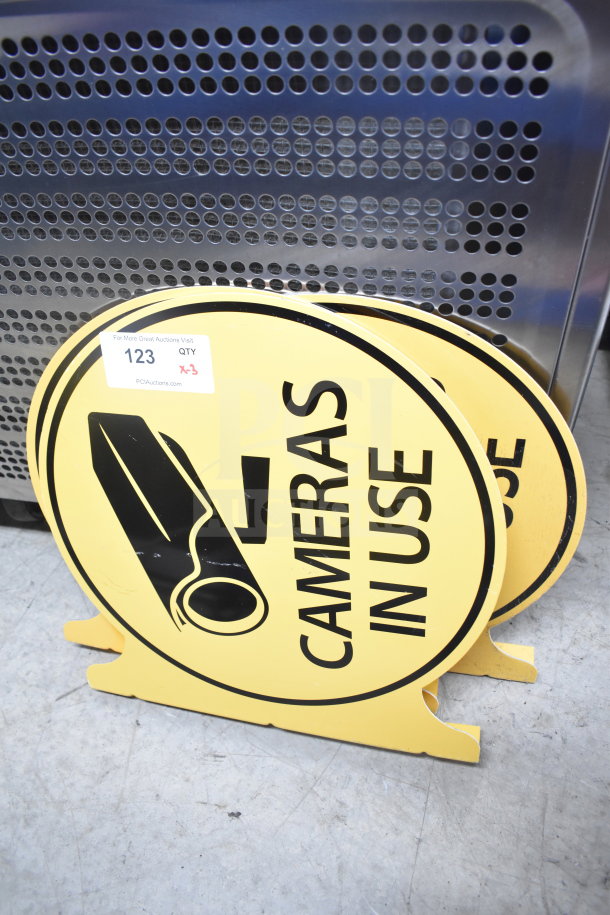 Three yellow "Cameras In Use" signs with black camera graphic. Includes auction label: Lot 123, quantity 3.