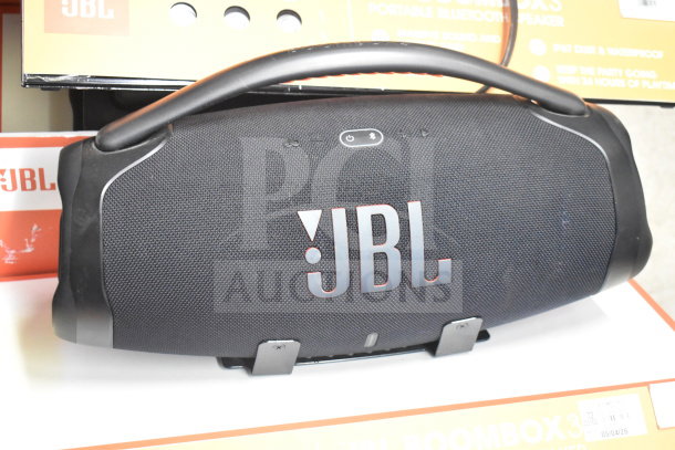 JBL Boombox speaker display, black mesh, sturdy handle, excellent condition, with JBL branding and packaging visible.