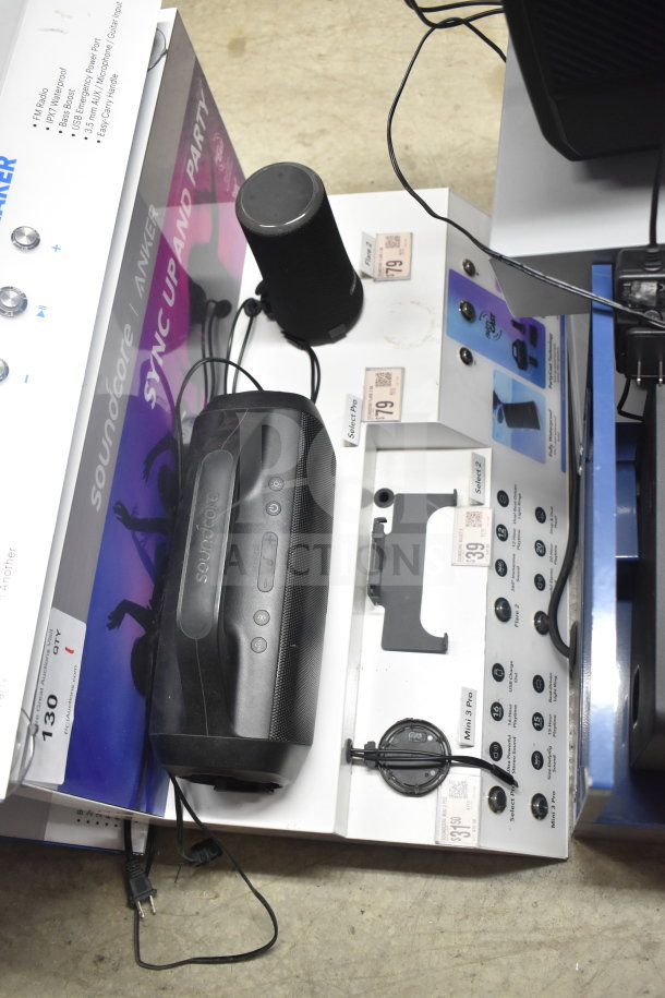 Store display featuring Soundcore Anker Select Pro speaker, showcasing controls and charging setup. Includes marketing graphics.