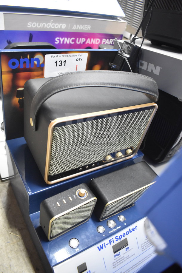 Store display featuring black Wi-Fi speaker set with gold accents, knobs, and grill. Includes Anker and onn. branding.