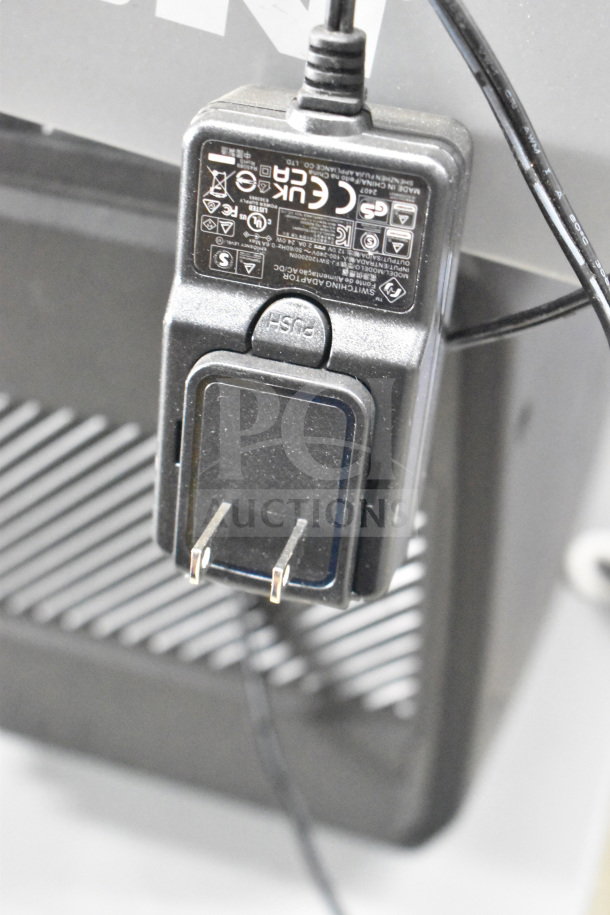 Plugged-in power adapter for a store display, visible labels with electrical specifications and compliance symbols.