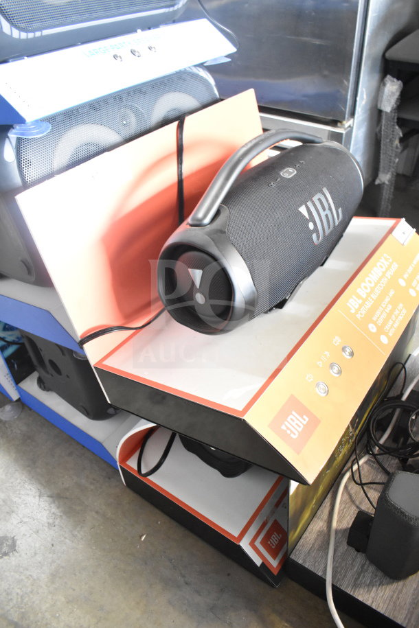 JBL Boombox 3 speaker on store display, features large handle, black mesh exterior, visible JBL branding and function buttons.