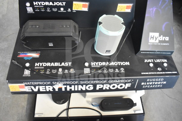 Two Altec Lansing store display speakers: black HydraJolt IMW1200 and teal HydraMotion IMW1100. Price tags visible.