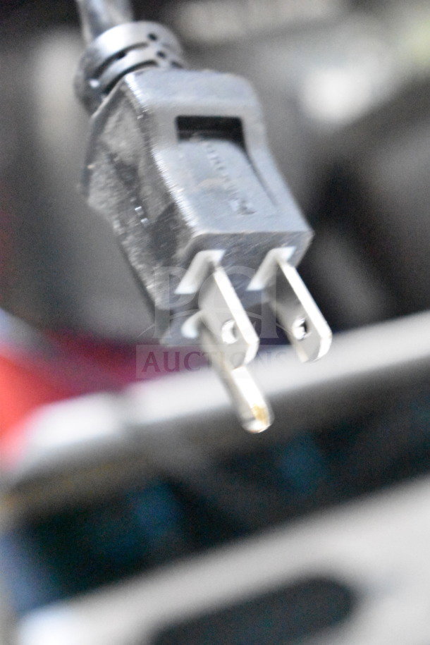 Close-up of a black power plug against a blurry background, part of a store display including Altec Lansing and Soundcore speakers.