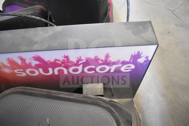 Altec Lansing and Soundcore speaker display with vibrant backdrop featuring crowd silhouette. Signs highlight the brands.