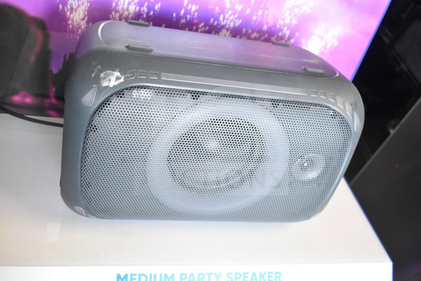 Onn Medium Party Speaker on display stand. Black casing, front speaker grille, moderate wear. Text below: "MEDIUM PARTY SPEAKER."