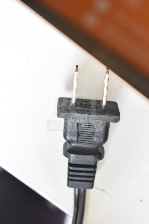 Power plug for the JBL Boombox 3 speaker, showing prongs and black plastic casing, near a white surface.