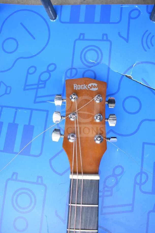 RockJam guitar headstock with tuning pegs on blue background. Visible RockJam logo. Appears in good condition.