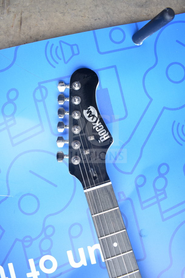Rock Jam guitar headstock with logo, six tuning pegs, in excellent condition on a blue background.