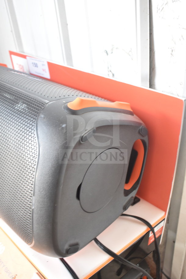JBL Partybox 110 speaker on store display, showcasing its portable design with orange accents. Cables are connected.