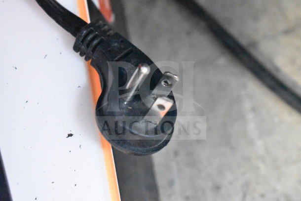 Close-up of an electrical plug attached to a JBL speaker in a display setup. The plug is black and has three prongs.