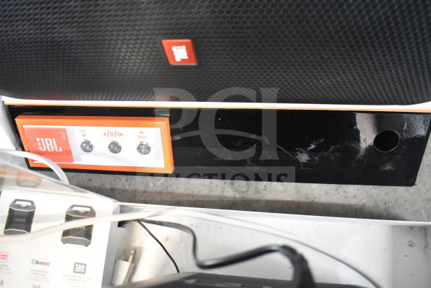 JBL speaker display with control panel. Features volume and playback buttons. Slight wear on housing.