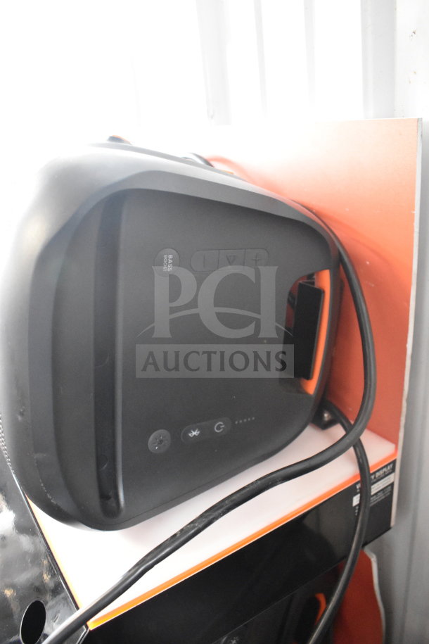 JBL speaker on display, black panel with control buttons and "BASS BOOST" label, cords visible, store display unit.