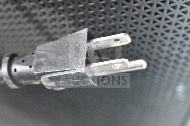 Close-up of a power plug against the textured surface of a store display, including JBL Partybox 310.